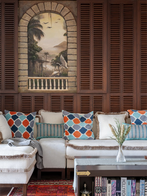 The lounge is a warm and inviting space, with a reused louvred backdrop from the family’s previous home. It features commissioned mural artwork by artist Sakpal - Beautiful Homes