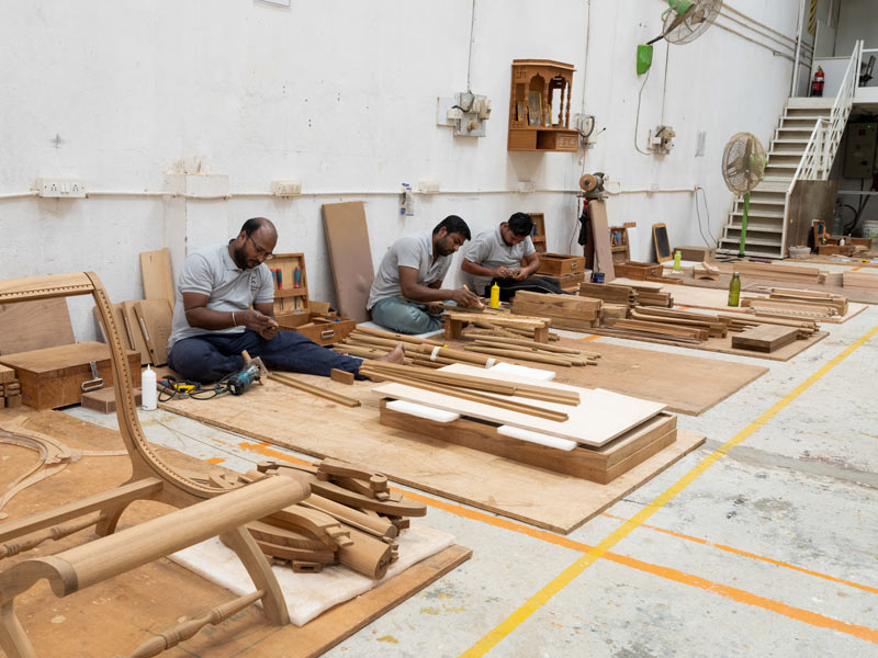 A Bentota Lounge Chair frame sits ready for polishing and caning, surrounded by carpenters – Beautiful Homes