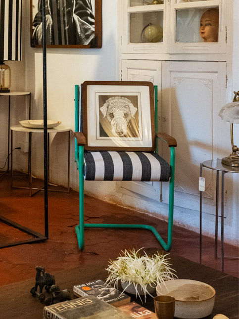 An eclectic interior featuring a green-framed chair with striped upholstery, a dog sketch, vintage white cabinetry – Beautiful Homes