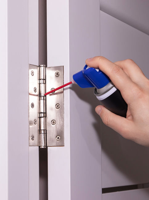 Person spraying lubricant oil on door hinge – Beautiful Homes