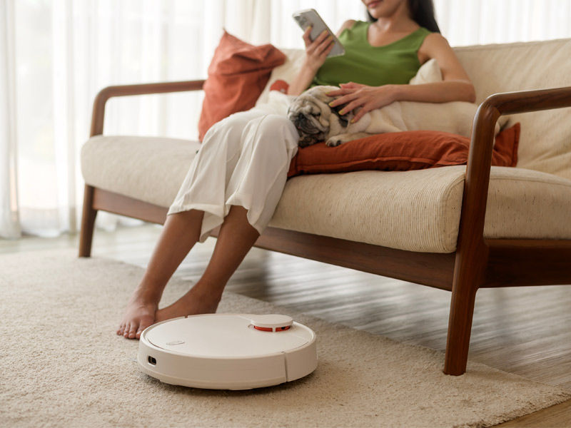 Robotic vacuum cleaner cleaning carpet near sofa with woman and dog – Beautiful Homes