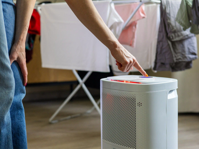 A person operating a portable dehumidifier in a room with drying laundry to reduce moisture – Beautiful Homes