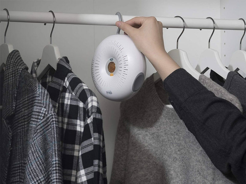 A hand holding a circular, rechargeable dehumidifier device inside a wardrobe to prevent musty odors – Beautiful Homes