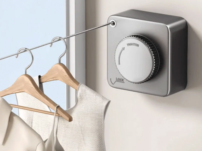 A wall-mounted retractable clothesline unit with the line extended, holding clothes on hangers – Beautiful Homes