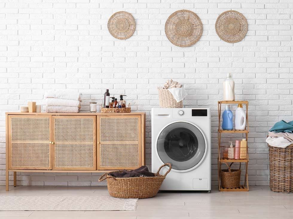Modern laundry room with a front-loading washing machine, wicker laundry baskets, detergent on a shelf, and white brick wall décor – Beautiful Homes