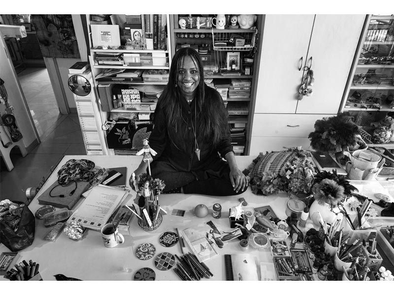 Mithu Sen smiling at her eclectic studio workspace filled with art supplies and curiosities – Beautiful Homes