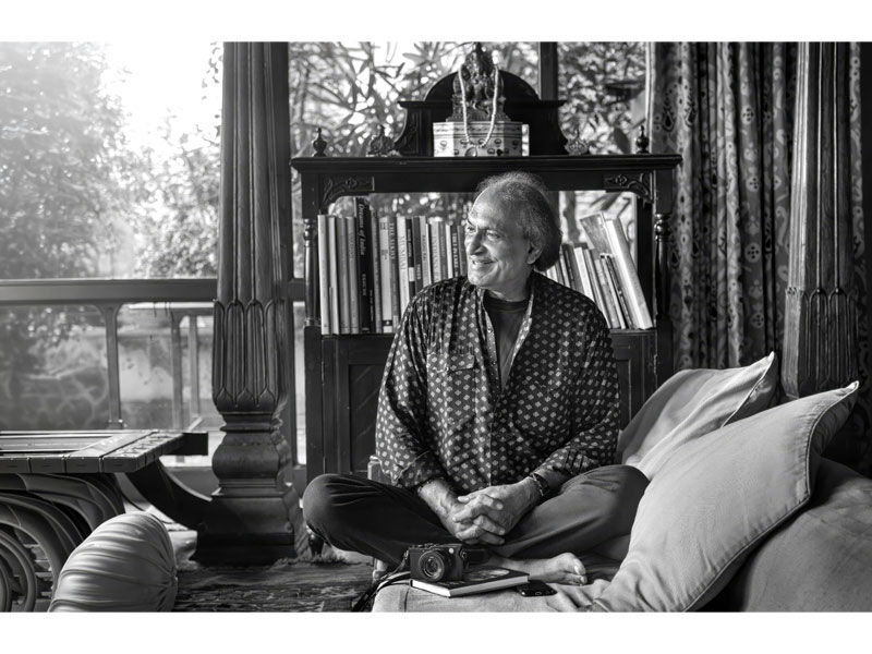 Raghu Rai seated at home with his camera and bookshelf – Beautiful Homes