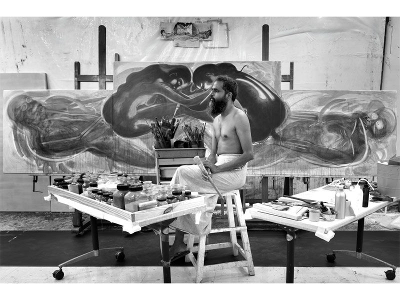 T Venkanna seated before a large-scale painting in his studio – Beautiful Homes