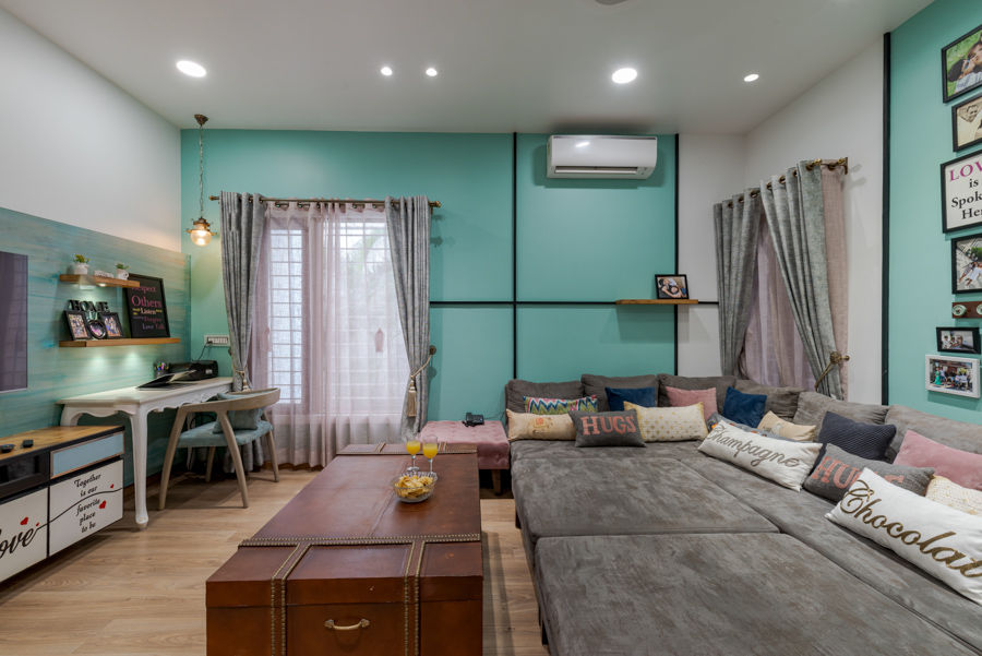 Family room design with teal walls, cushions in pastel hues, a grey couch-bed and a vintage desk