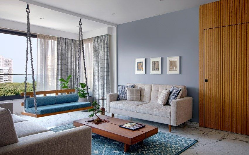 Nautical family room design with wood door and coffee table, swing in front of big window, off-white couches
