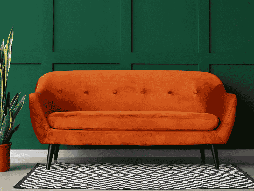 Bold Interior With An Orange MidCentury Modern Sofa, Dark Green Wall, And Geometric Rug - Beautiful Homes