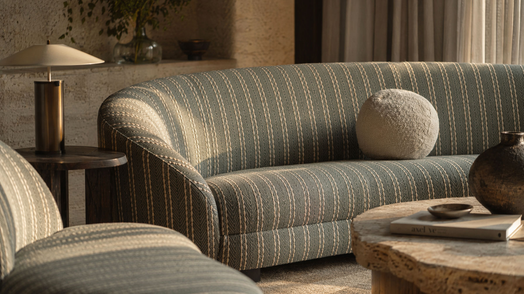 Curved sofa furnishing with muted green and beige striped upholstery, rounded backrest, and sculptural form - Beautiful Homes