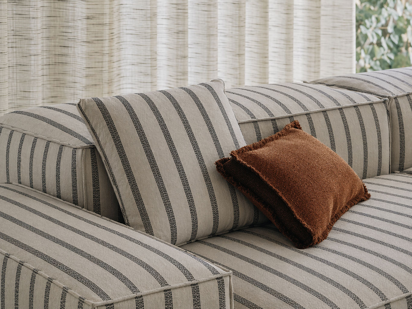 Low-profile modular sofa in beige striped upholstery with a matching cushion and rust textured accent pillow, styled in a soft contemporary interior - Beautiful Homes