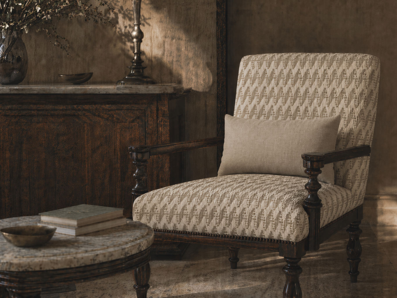 Upholstered armchair with a cream and beige geometric jacquard pattern, solid taupe lumbar cushion, and dark carved wooden frame - Beautiful Homes