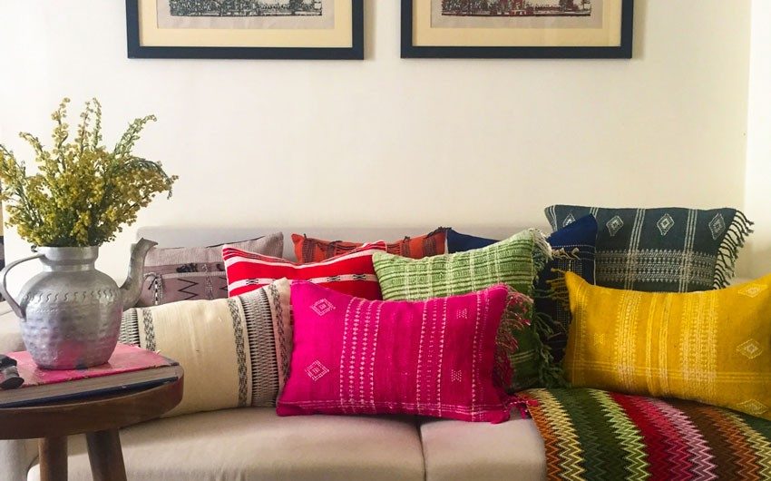 A sofa with a number of cushions fitted with Gyasar cushion covers and in front of it is a side table with a cutlery set
