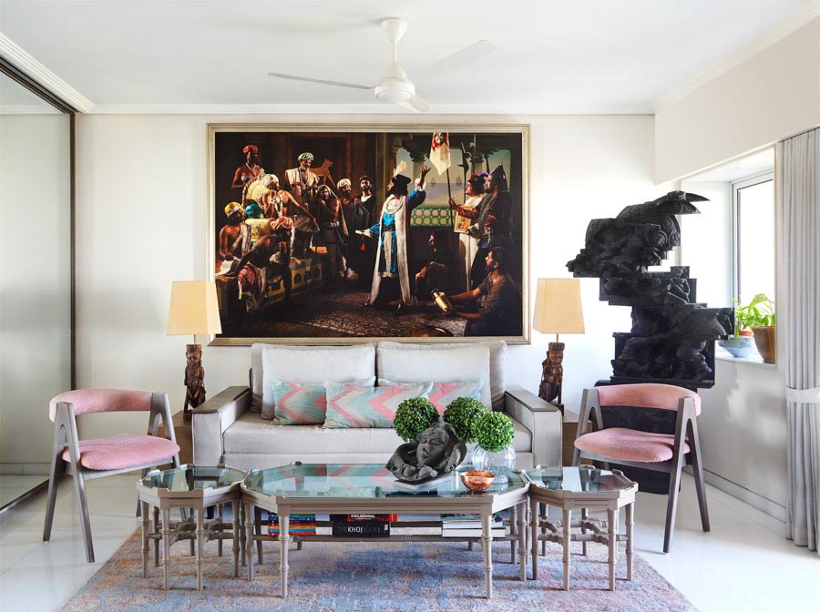Living room with a white sofa, glass coffee table, two identical pink chairs and a large artwork on the wall behind the sofa