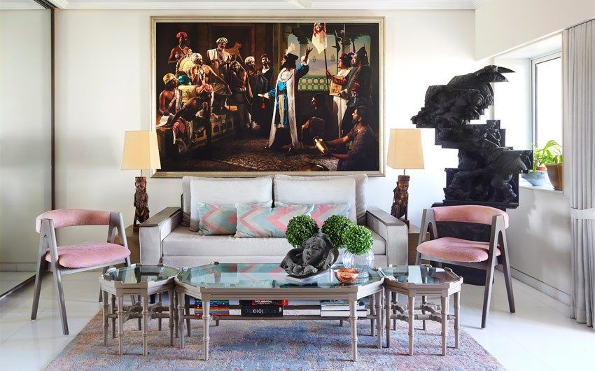Living room with a white sofa, glass coffee table, two identical pink chairs and a large artwork on the wall behind the sofa - Beautiful Homes