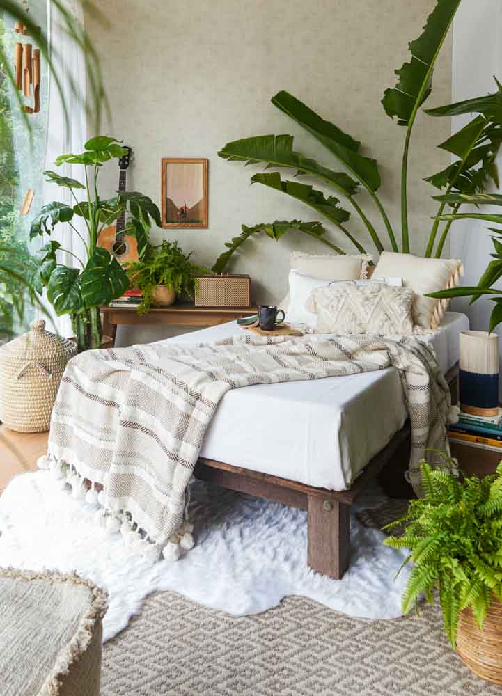 A single bed in a white bedroom with plants, a table, a guitar and a radio