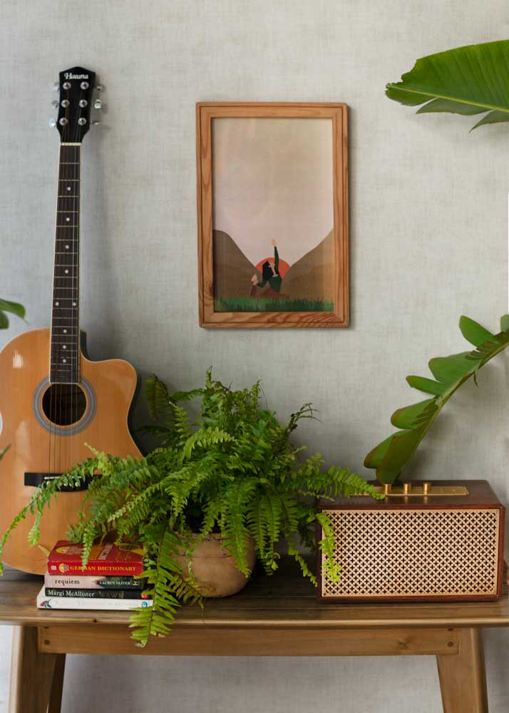 A guitar and a radio placed on a small wooden table with an artwork hung on the wall behind