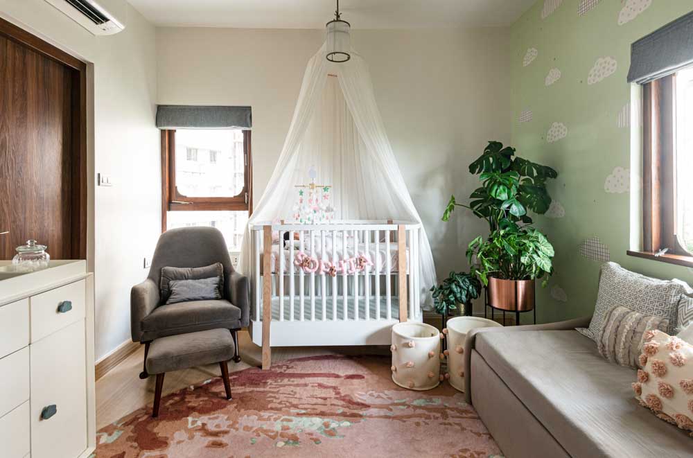 A room with a white wooden cot, a planter, a rug, a mosquito net and a grey chair