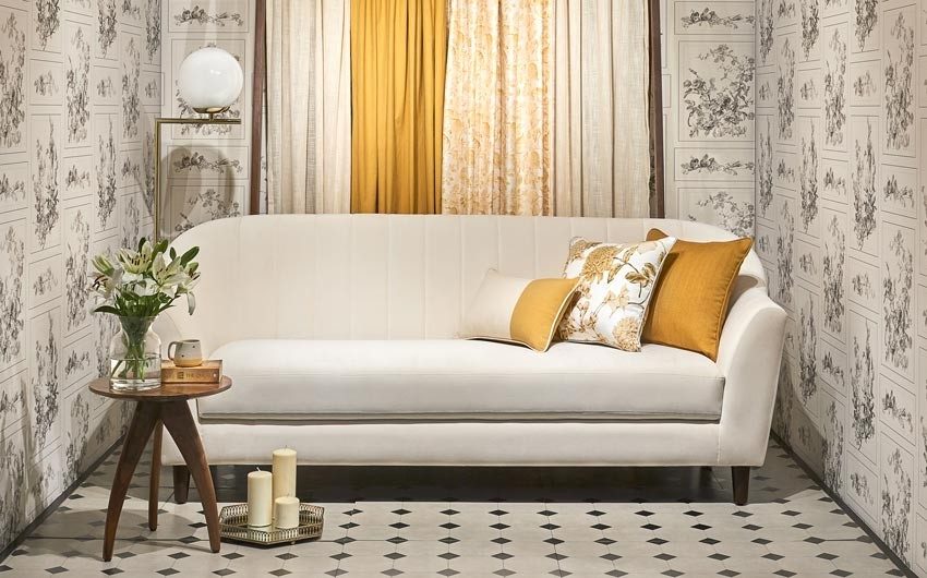 A wallpapered room with a white sofa, a side table with a planter and a lamp behind the sofa