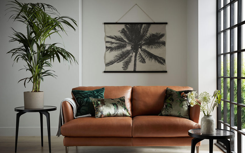 A white room with a brown sofa, a couple of side tables with planters on them and an artwork on the wall behind the sofa