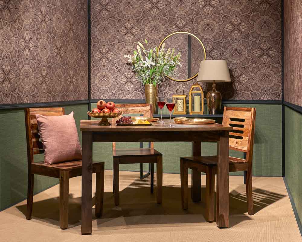 A wooden dining table with three chairs placed in a wallpapered room