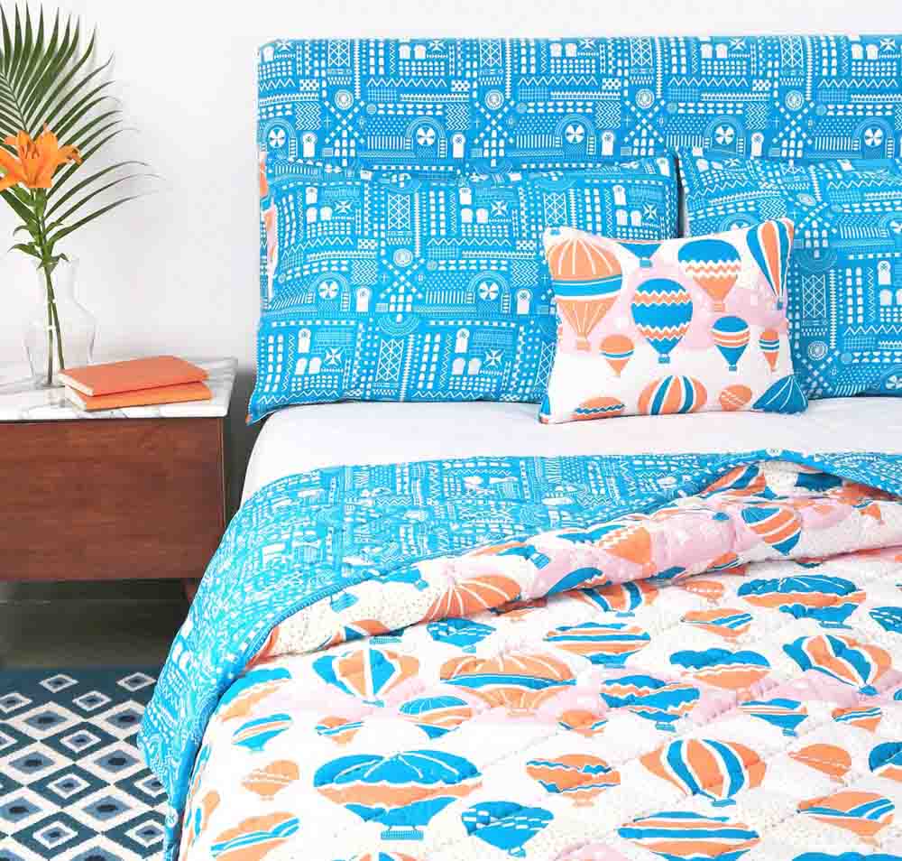 A blue quilt, with hot air balloons printed on it placed on a bed with a sidetable besides it