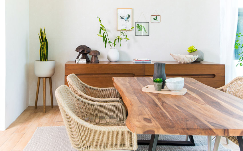 Live edge dining table in a living room with a modern wooden cabinet, cane chairs, wooden floor and a few plants
