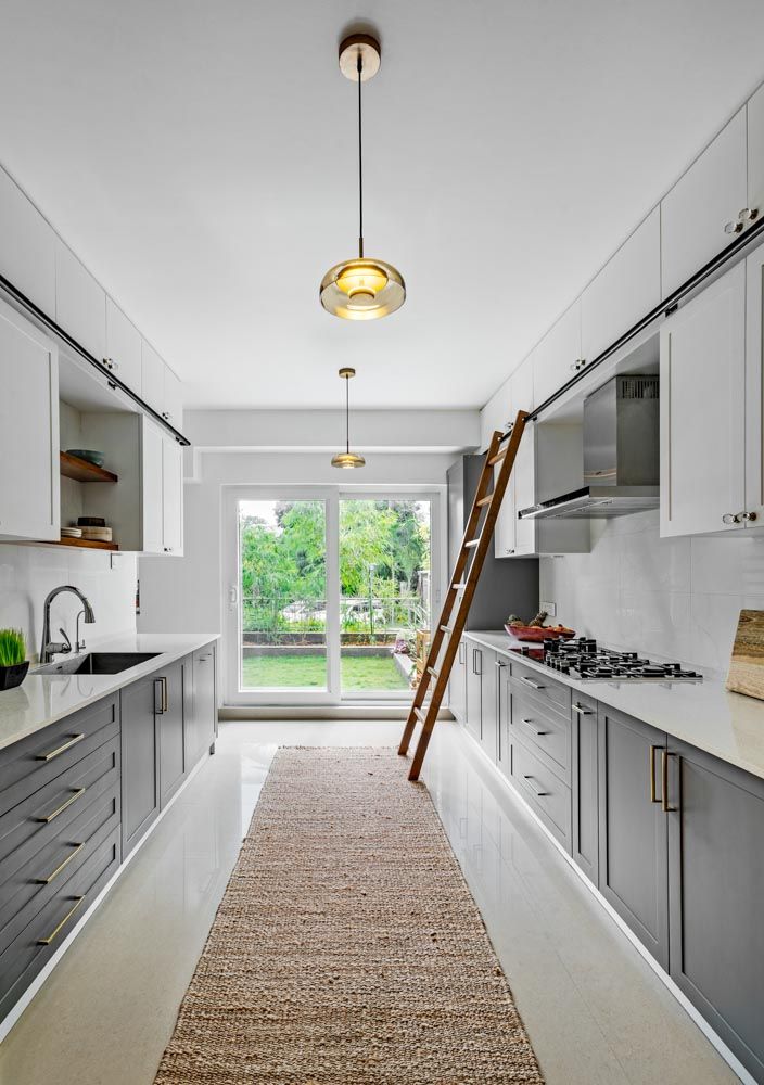 Parallel modular kitchen with white & grey colour palette with windows opening to garden - Beautiful Homes