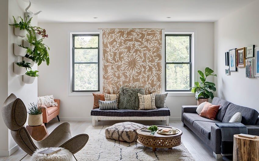 A white living room with a tapestry hung on a wall, a blue sofa, a bench with cushions, a grey chair and some plants on a wall - Beautiful Homes