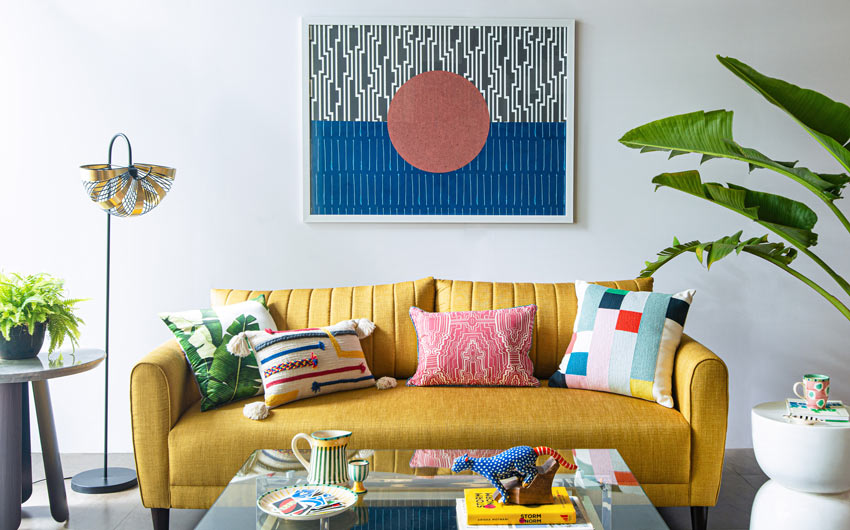 A Living room setting with a yellow sofa, arm chairs, coffee table, carpets, lamp and artwork