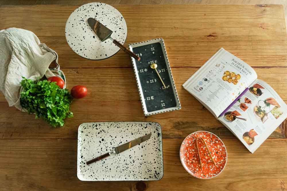 A wooden countertop with ceramic cutlery, a recipe book and some vegetables