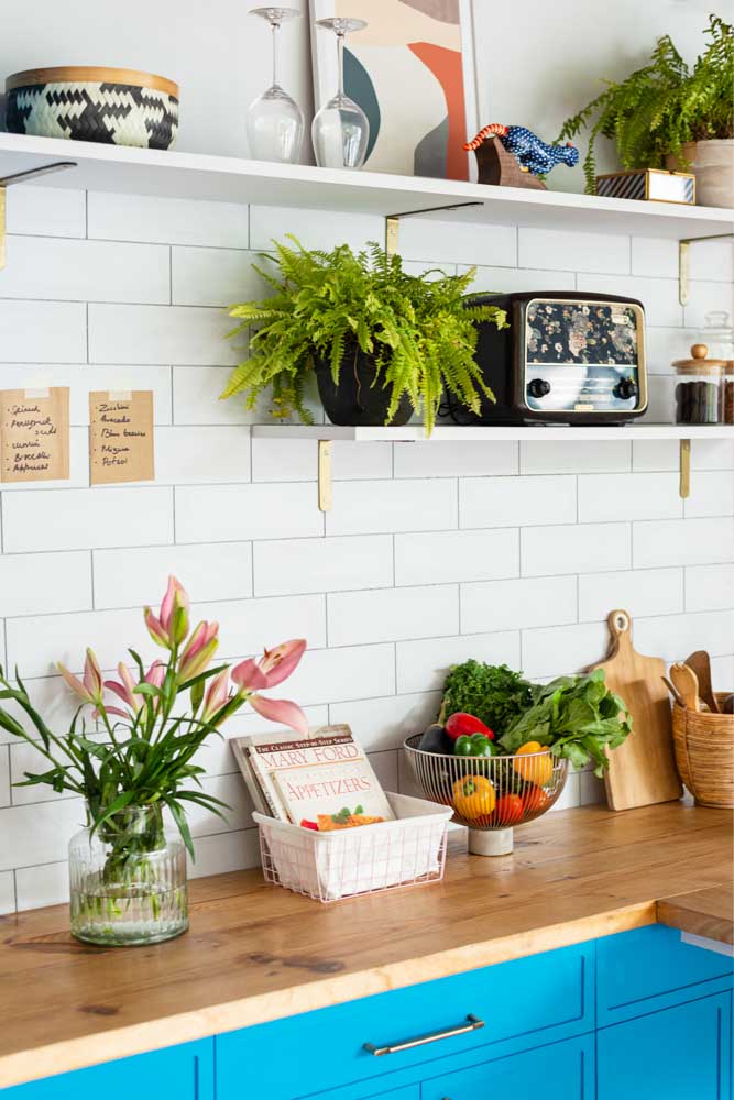A kitchen with two wooden shelves where there is a flower vase, a basket, a radio and some planters