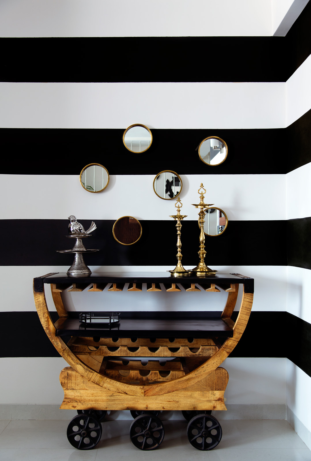 Wooden bar with wheels and a bold striped wall with little mirrors in Avilasha Barroah's home