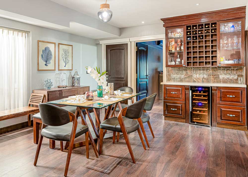  A six seater glass top dining table in a dining room with wooden flooring and a wine cabinet
