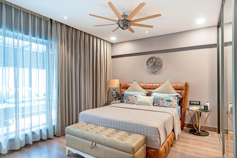 A bedroom with a large bed with along with two side tables, a clock, wooden flooring and a ceiling fan