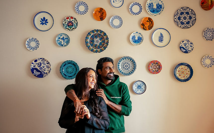 Remo D’Souza & his wife Lizelle standing in front of their wall adorned with wall plates - Beautiful Homes