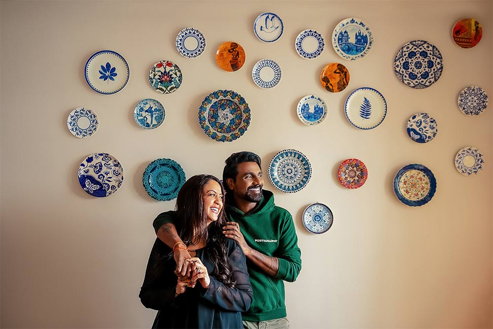 Remo D’Souza & his wife Lizelle standing in front of their wall adorned with wall plates - Beautiful Homes