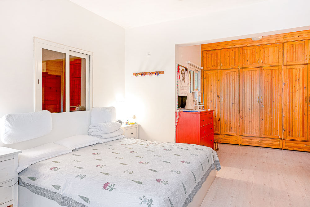  A bedroom with a large double bed, a small red cabinet and. a large wooden wardrobe fixed to the wall