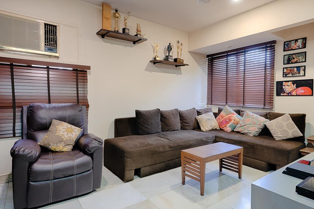 Saqib’den with brown L-shaped sofa, leather lounge chair, and subtle floral wallpaper