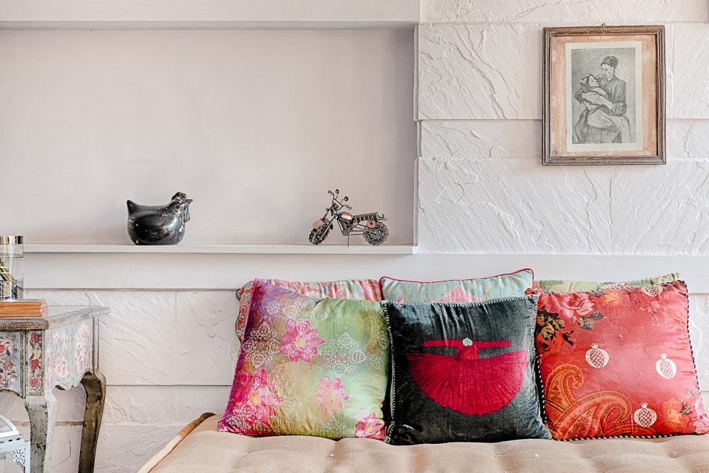 Colourful and quirky cushions on a sofa in the living area on a textured white wall with framed art