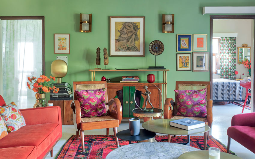 A living room with a green wall and an orange and a pink sofa facing each other