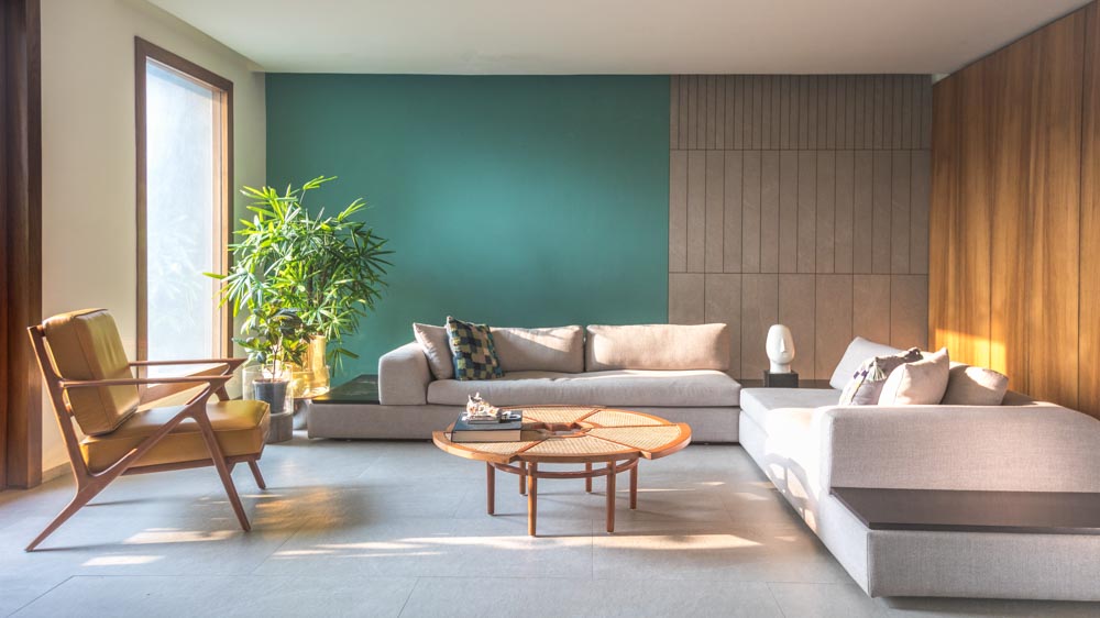 A green living room with a large grey sofa  and a rattan centre table
