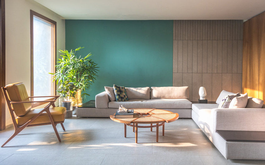A green living room with a large grey sofa  and a rattan centre table