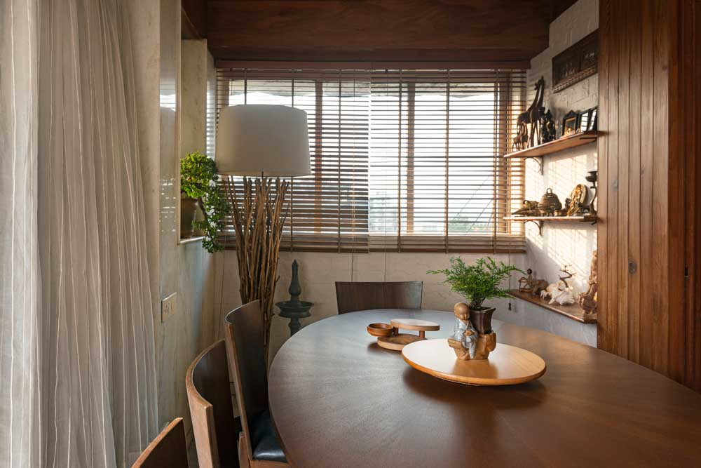 A dining area with an oval shaped wooden dining table and a lamp in one corner