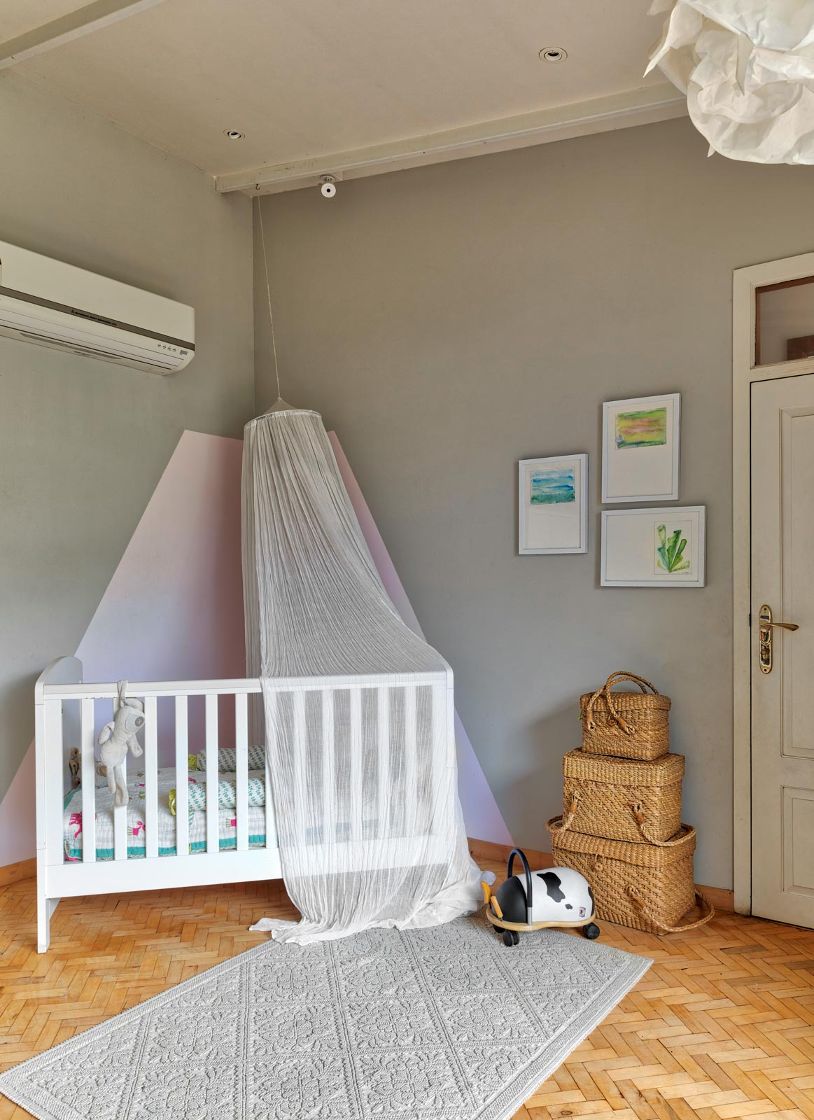 Nursery with white crib, grey and pink wall, little décor and warm parquet