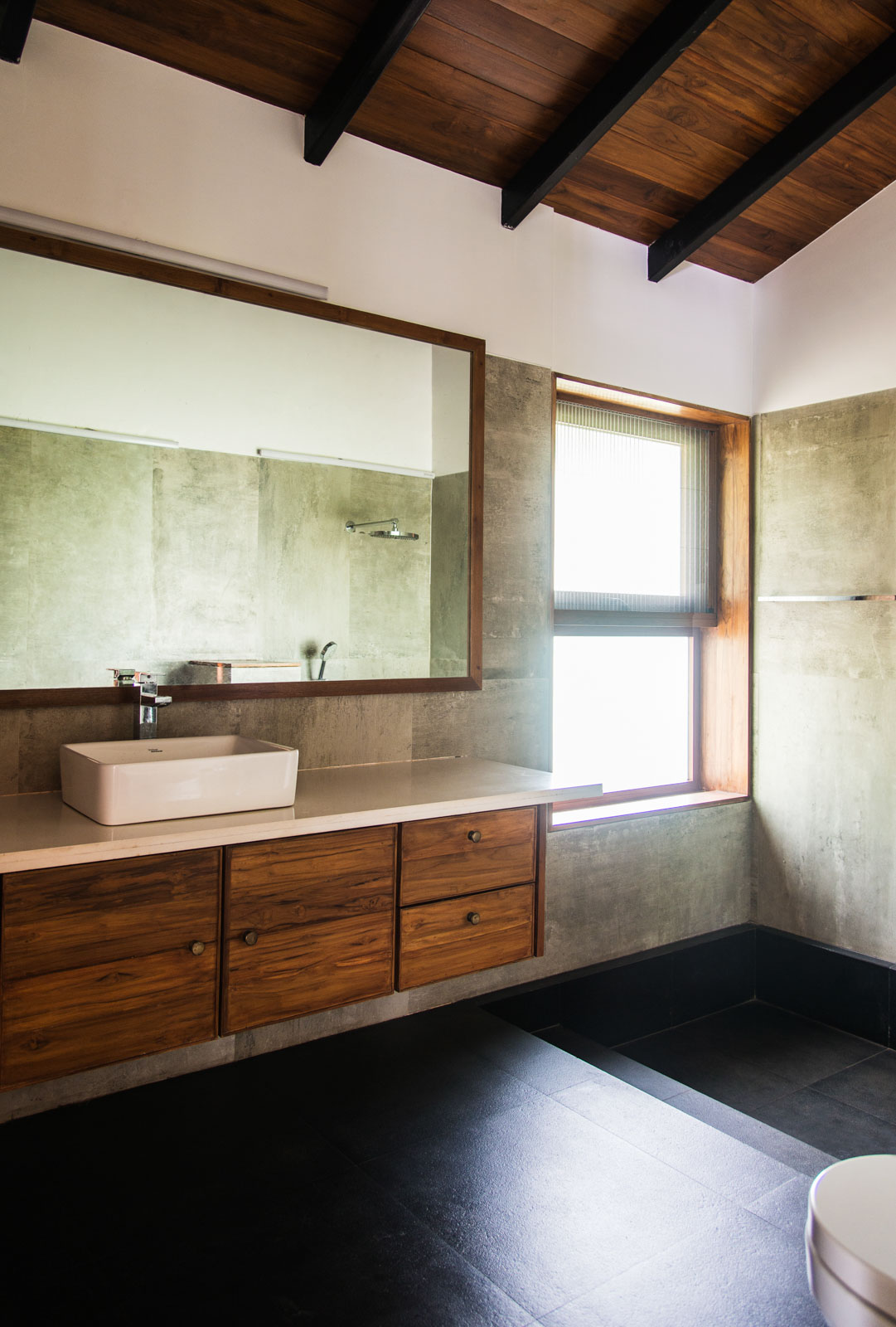 Minimalistic bathroom with wooden storage and big mirror, dark floor and one window