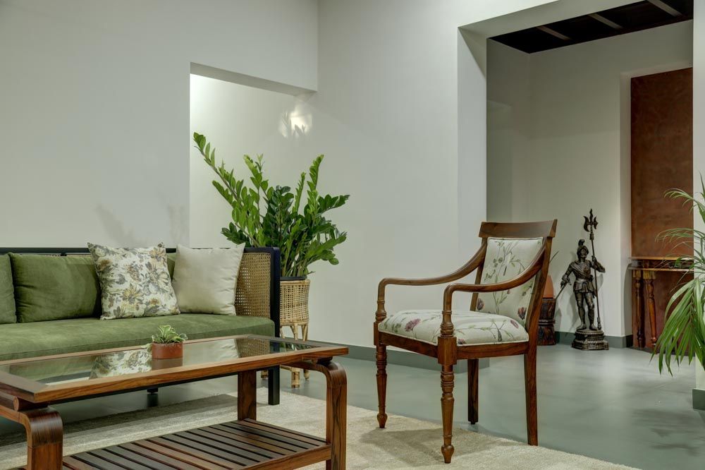 A white living room with a wooden sofa with green fabrics and a floral chair - Beautiful Homes