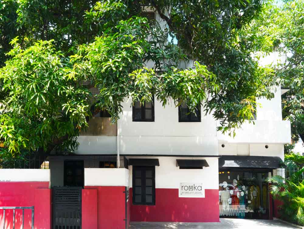 A 2 storeyed building painted in white and red with a mango tree in front of it - Beautiful Homes
